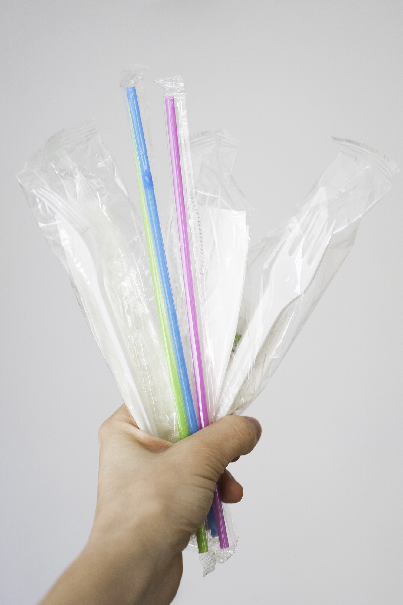 Hand holding plastic straws and single use cutlery